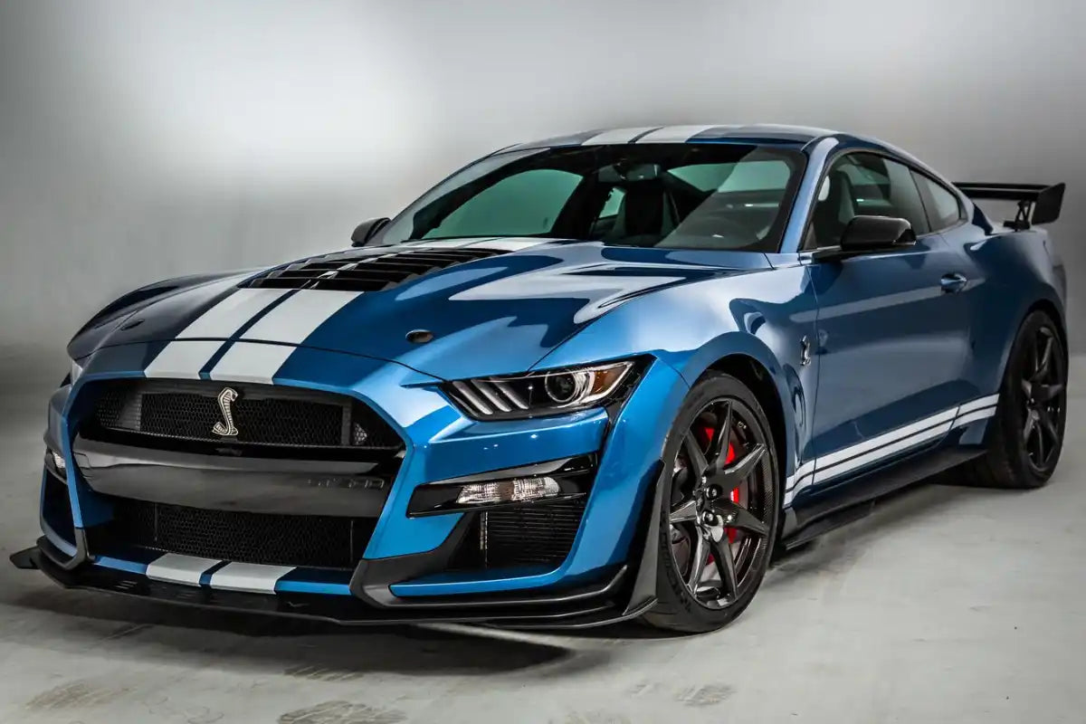 Blue Ford Mustang Shelby GT500 with white racing stripes and aggressive aerodynamic bodywork.