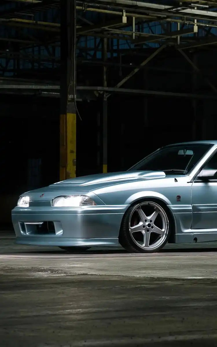 Modified silver Nissan Skyline R32 with aftermarket wheels and body kit.