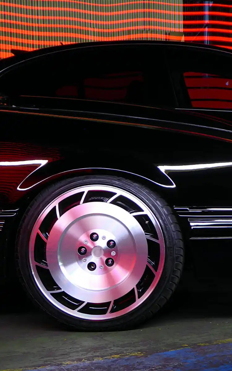 Sleek black car wheel with distinctive silver turbine-style rims illuminated by pink lighting.